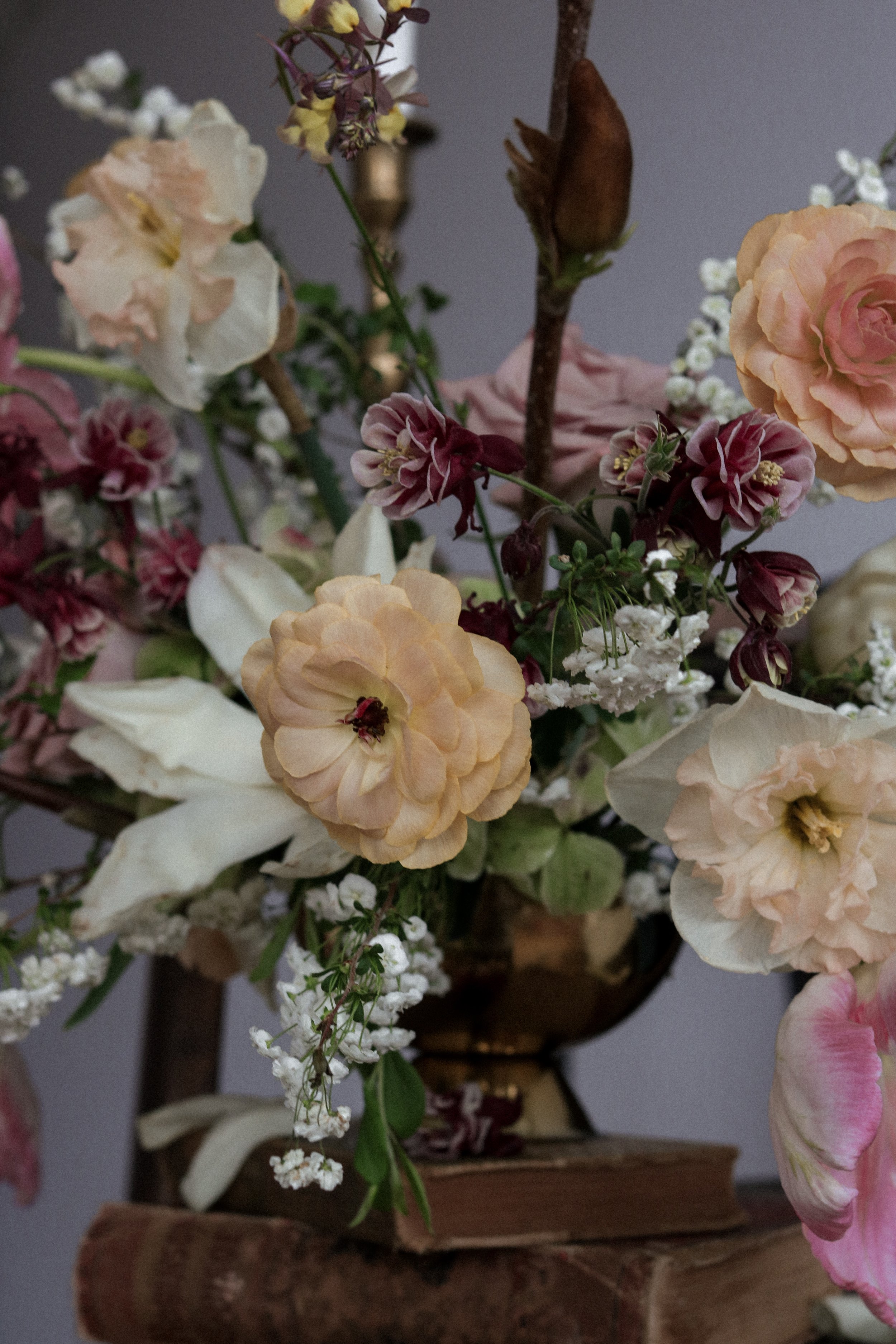 A bouquet of various flowers including cream-colored roses, white lilies, small white and pink blossoms, and purple flowers arranged in a dark vase on a wooden surface.